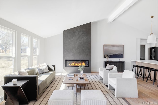 living room with lofted ceiling with beams, a large fireplace, light wood-style flooring, and baseboards