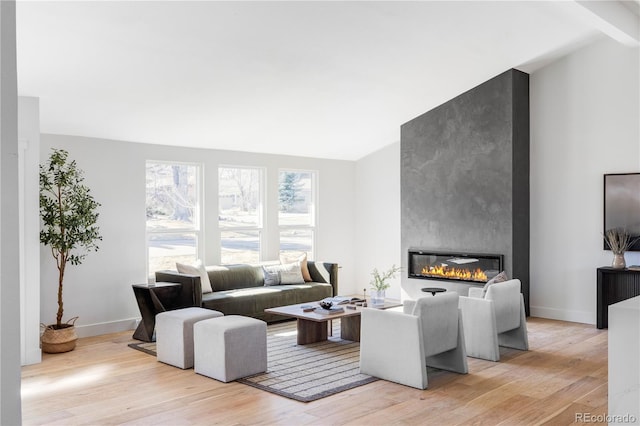 living area featuring a large fireplace, vaulted ceiling, light wood-type flooring, and baseboards