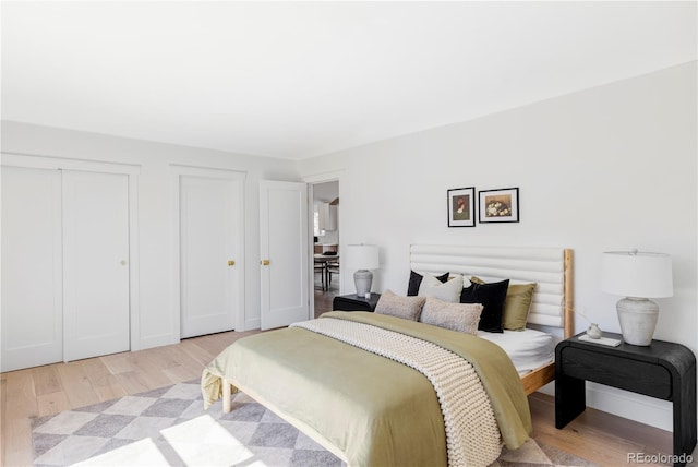 bedroom featuring light wood-style flooring, baseboards, and two closets