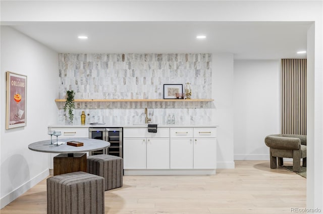 bar featuring baseboards, wine cooler, wet bar, light wood-style floors, and a sink