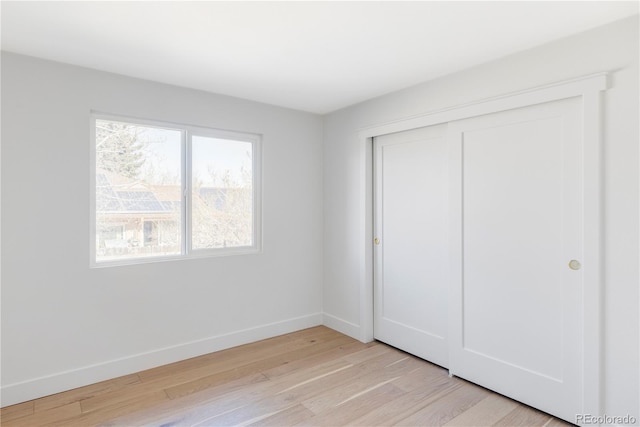 unfurnished bedroom featuring light wood-style floors, baseboards, and a closet