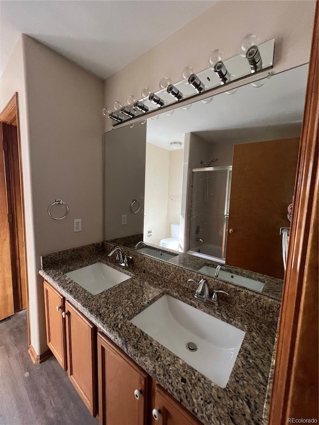 full bathroom featuring wood finished floors, double vanity, toilet, and enclosed tub / shower combo