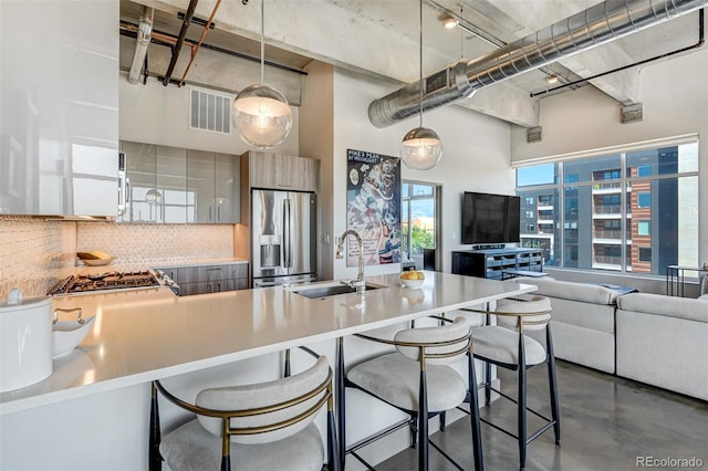 kitchen featuring pendant lighting, sink, decorative backsplash, a towering ceiling, and stainless steel fridge