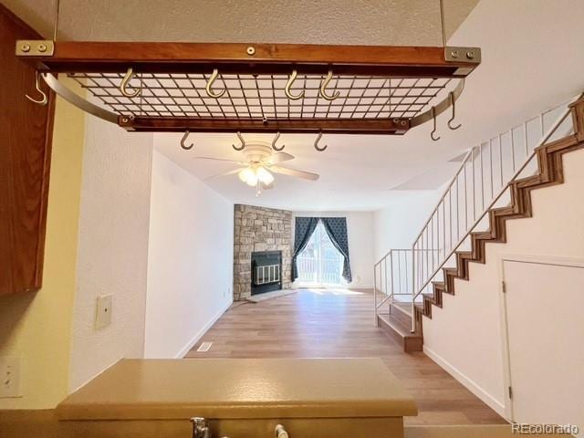 stairs featuring baseboards, a stone fireplace, wood finished floors, and ceiling fan