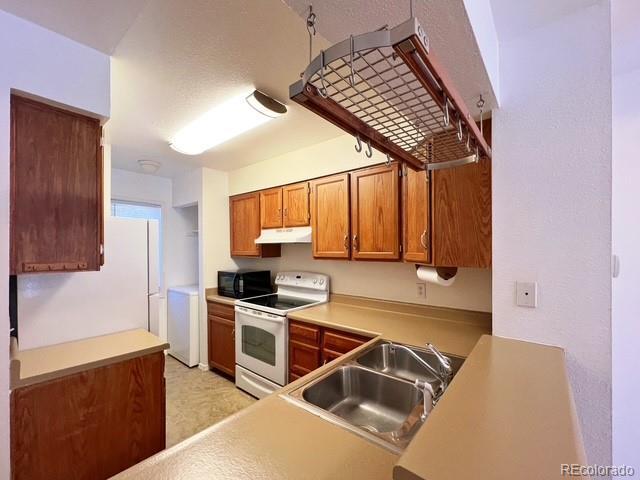 kitchen featuring black microwave, under cabinet range hood, brown cabinetry, white range with electric stovetop, and a sink