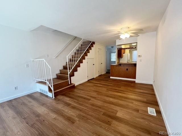 unfurnished living room featuring stairway, baseboards, a ceiling fan, and dark wood finished floors