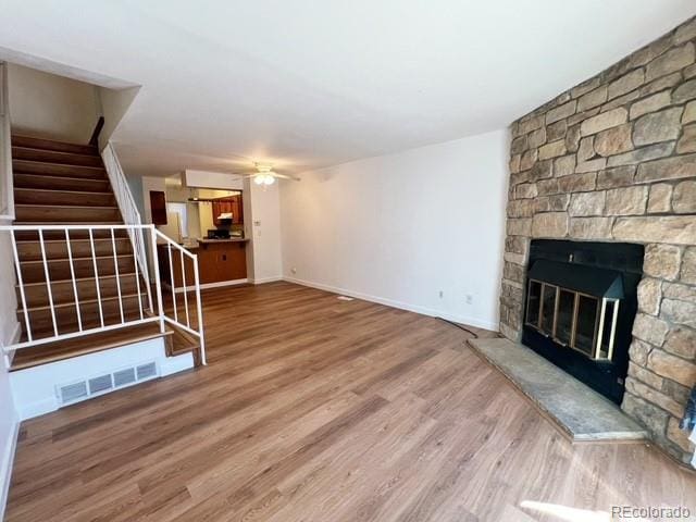 unfurnished living room featuring a fireplace, stairs, visible vents, ceiling fan, and wood finished floors
