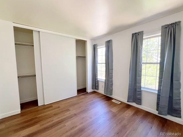unfurnished bedroom featuring baseboards, multiple windows, and wood finished floors