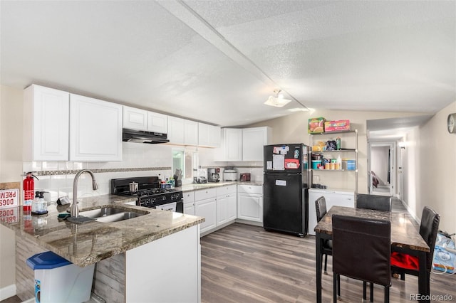 kitchen with lofted ceiling, under cabinet range hood, a peninsula, a sink, and black appliances