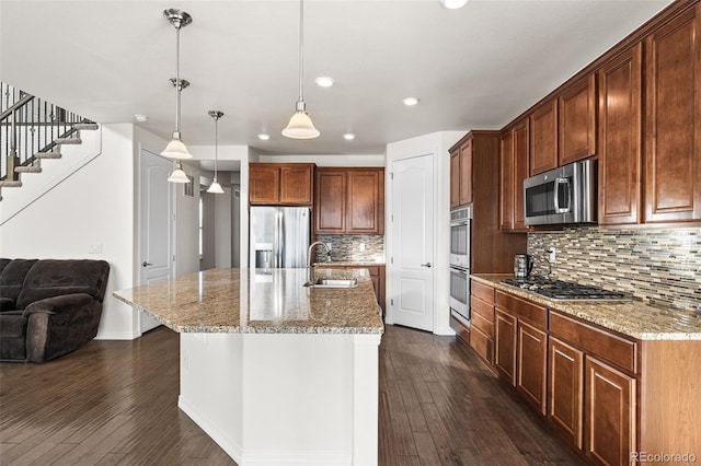 kitchen featuring pendant lighting, appliances with stainless steel finishes, light stone counters, and a center island with sink