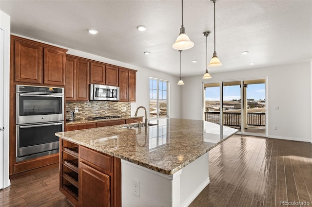 kitchen with sink, dark hardwood / wood-style flooring, an island with sink, pendant lighting, and stainless steel appliances