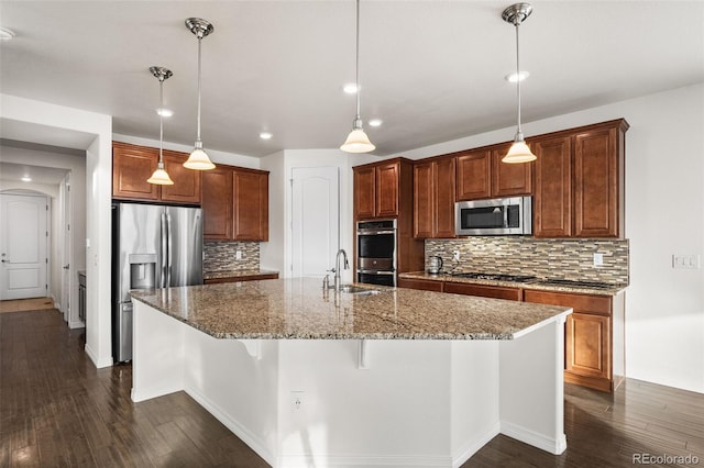 kitchen featuring appliances with stainless steel finishes, decorative light fixtures, a kitchen bar, dark stone counters, and a kitchen island with sink