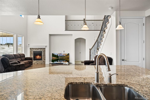 kitchen with a towering ceiling, pendant lighting, sink, light stone counters, and a textured ceiling