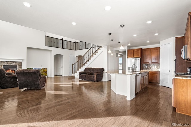 kitchen featuring pendant lighting, an island with sink, backsplash, stainless steel appliances, and dark wood-type flooring