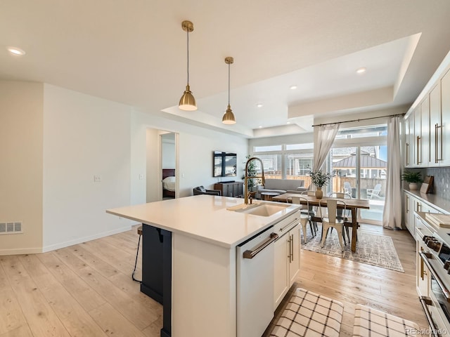 kitchen featuring dishwasher, light hardwood / wood-style floors, white cabinetry, and an island with sink