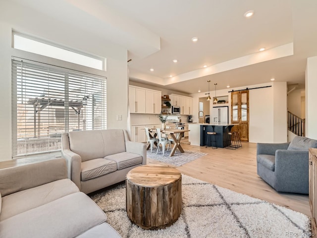 living room featuring a raised ceiling, a barn door, and light hardwood / wood-style flooring