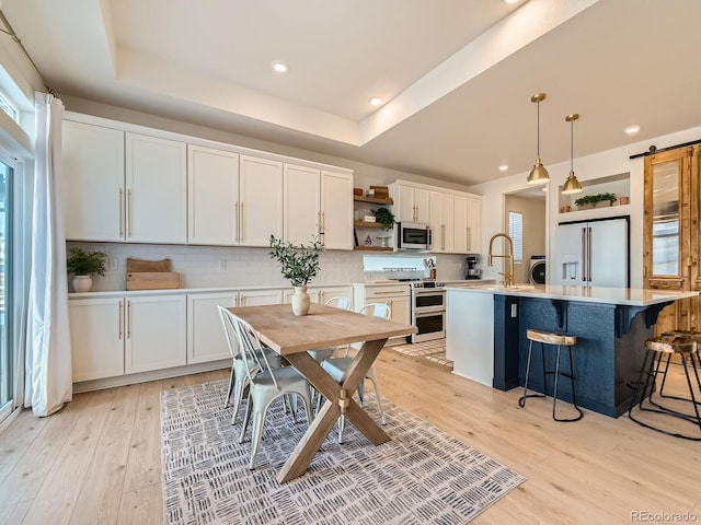 kitchen featuring stainless steel appliances, pendant lighting, a barn door, a center island with sink, and white cabinetry