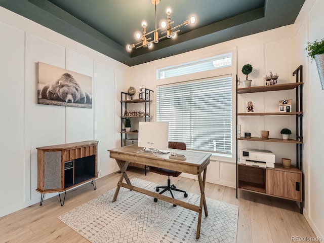 home office with an inviting chandelier, light hardwood / wood-style floors, a raised ceiling, and a wealth of natural light