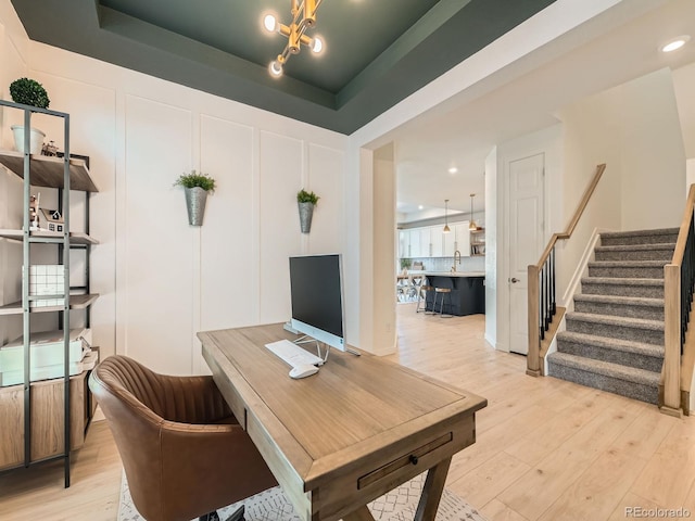 home office featuring a tray ceiling, light hardwood / wood-style flooring, and a notable chandelier