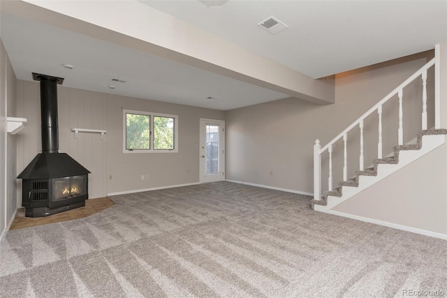 unfurnished living room featuring beamed ceiling, carpet, and a wood stove