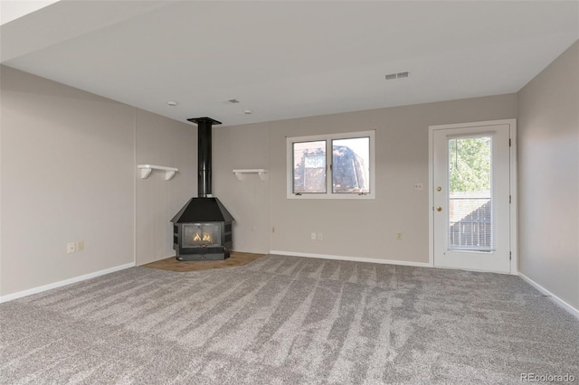 unfurnished living room with a healthy amount of sunlight, carpet, and a wood stove