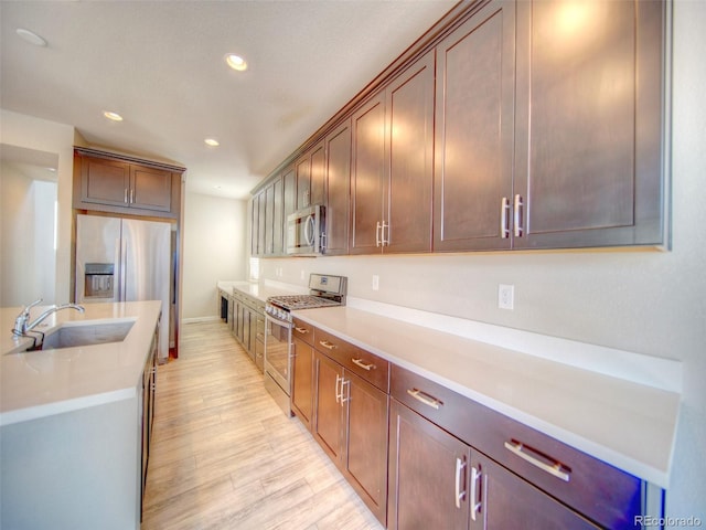 kitchen with appliances with stainless steel finishes, sink, and light hardwood / wood-style flooring