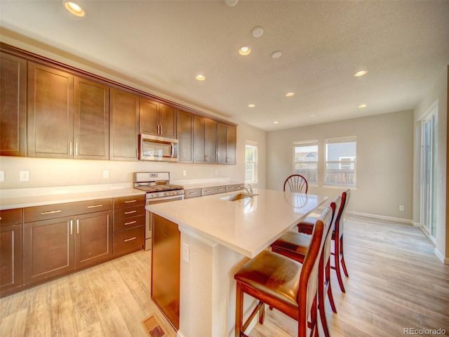 kitchen featuring sink, a kitchen island with sink, appliances with stainless steel finishes, a breakfast bar, and light wood-type flooring