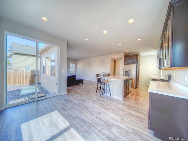 kitchen with light hardwood / wood-style flooring, an island with sink, appliances with stainless steel finishes, and a kitchen bar