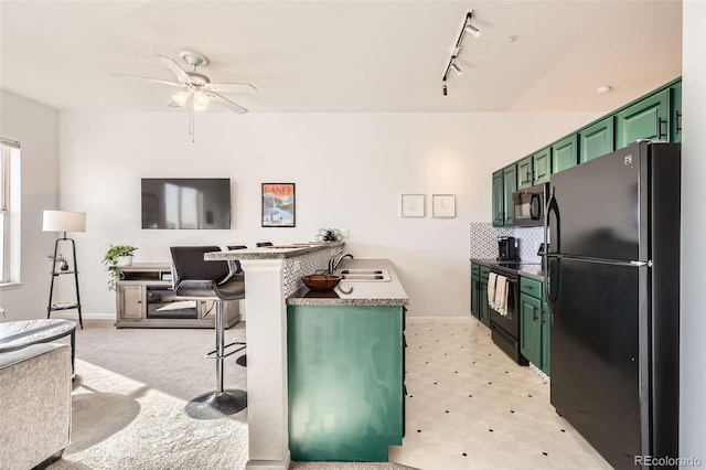 kitchen with a kitchen bar, rail lighting, a sink, black appliances, and green cabinetry