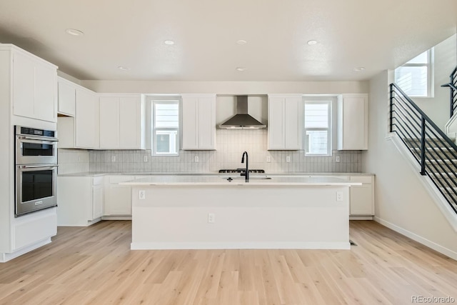 kitchen featuring a wealth of natural light, a center island with sink, stainless steel appliances, and wall chimney range hood