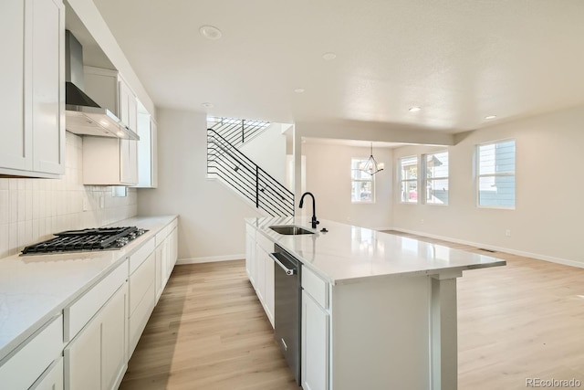 kitchen with light wood-type flooring, wall chimney exhaust hood, stainless steel appliances, sink, and white cabinetry