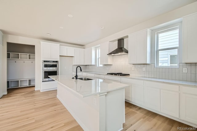 kitchen featuring a center island with sink, sink, wall chimney exhaust hood, light hardwood / wood-style floors, and stainless steel appliances