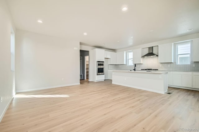 kitchen with a center island with sink, light hardwood / wood-style flooring, a wealth of natural light, and wall chimney exhaust hood