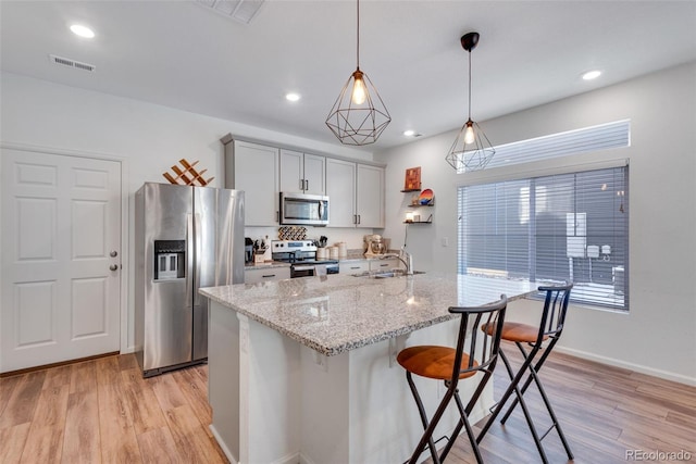 kitchen featuring a center island with sink, sink, decorative light fixtures, light stone counters, and stainless steel appliances