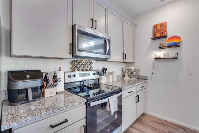 kitchen featuring white cabinets, light stone countertops, appliances with stainless steel finishes, and light hardwood / wood-style flooring