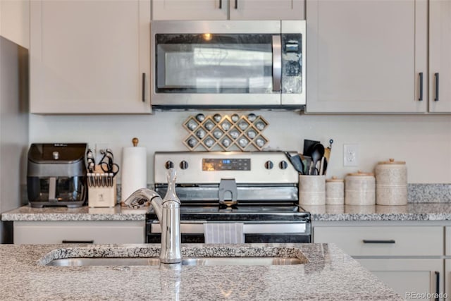 kitchen with light stone countertops, sink, white cabinets, and appliances with stainless steel finishes