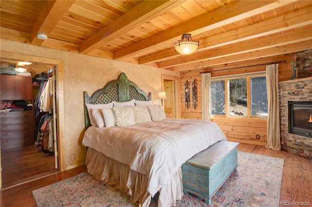 bedroom featuring a spacious closet, wood ceiling, hardwood / wood-style floors, a fireplace, and beamed ceiling