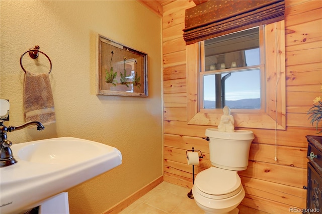 bathroom featuring sink, toilet, tile patterned floors, and wooden walls