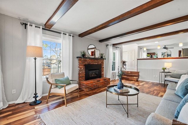 living room featuring ceiling fan, beam ceiling, a brick fireplace, and hardwood / wood-style floors