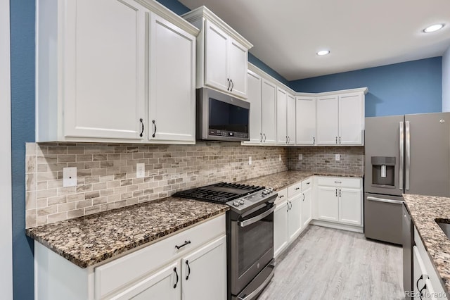 449 Vista Blvd, Lochbuie, CO 80603 - kitchen featuring stainless steel appliances, white cabinets, light wood finished floors, dark stone countertops, and recessed lighting