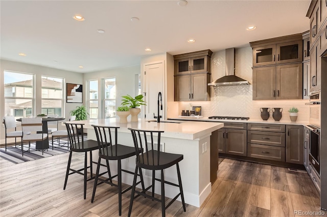 kitchen with a center island with sink, sink, wall chimney exhaust hood, appliances with stainless steel finishes, and dark hardwood / wood-style flooring