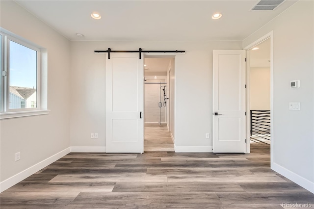 unfurnished bedroom with hardwood / wood-style floors and a barn door