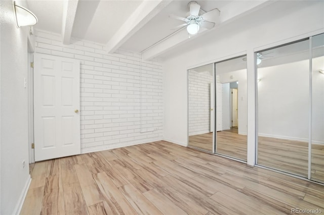 unfurnished bedroom featuring two closets, beamed ceiling, light wood finished floors, ceiling fan, and brick wall