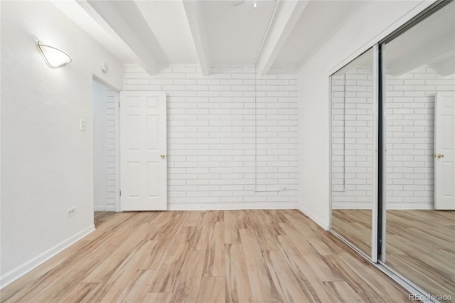 unfurnished bedroom with beamed ceiling, a closet, light wood-style flooring, and baseboards