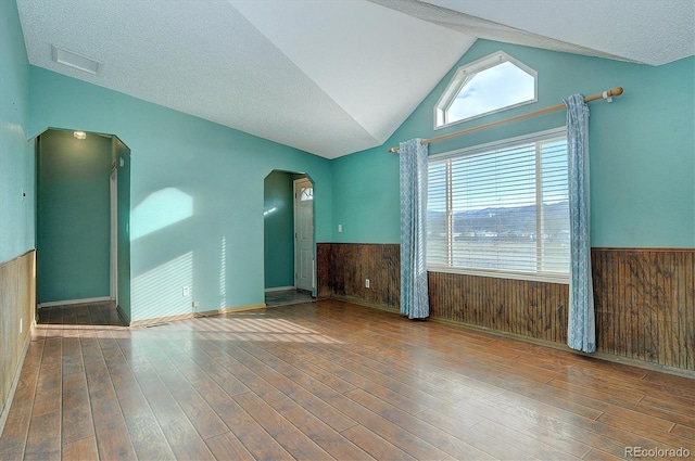 unfurnished room with lofted ceiling, a textured ceiling, wooden walls, and wood-type flooring