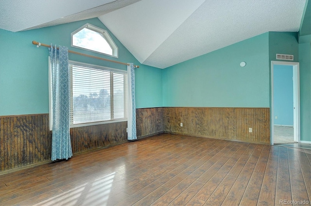 empty room featuring hardwood / wood-style flooring, lofted ceiling, a textured ceiling, and wooden walls