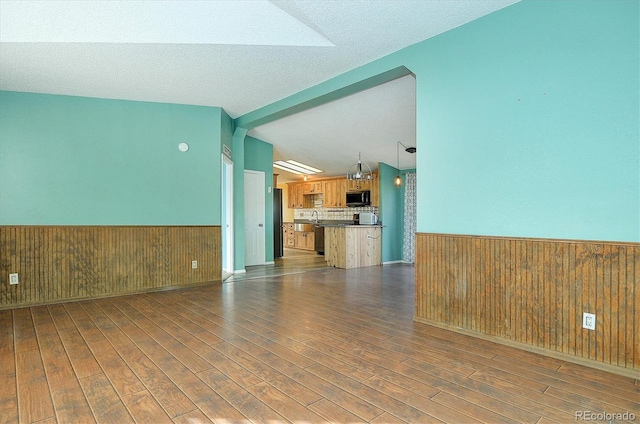 unfurnished living room featuring dark hardwood / wood-style floors, vaulted ceiling with beams, sink, and wooden walls