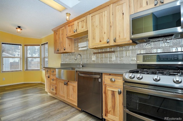 kitchen featuring sink, crown molding, light hardwood / wood-style flooring, appliances with stainless steel finishes, and decorative backsplash