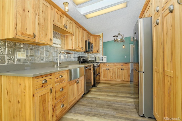 kitchen with appliances with stainless steel finishes, sink, decorative backsplash, light hardwood / wood-style floors, and a textured ceiling