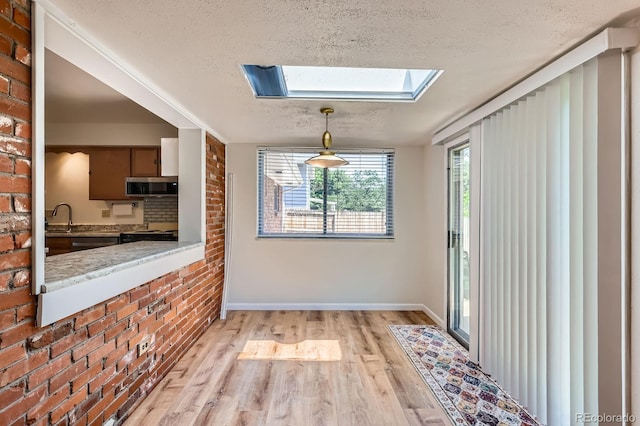 912 S Kingston St, Aurora, CO 80012 - unfurnished dining area featuring a textured ceiling, a skylight, light wood finished floors, brick wall, and a sink